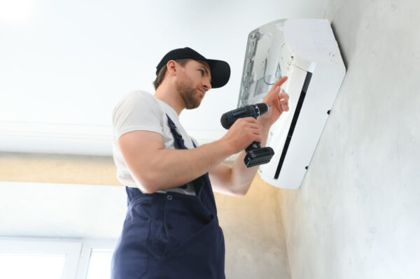 Pracownik w trakcie montażu klimatyzacji na ścianie.