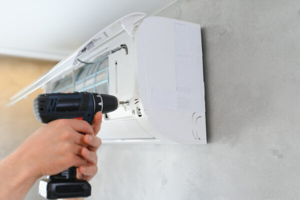 Ręka trzymająca wiertarkę podczas montażu klimatyzacji na ścianie.