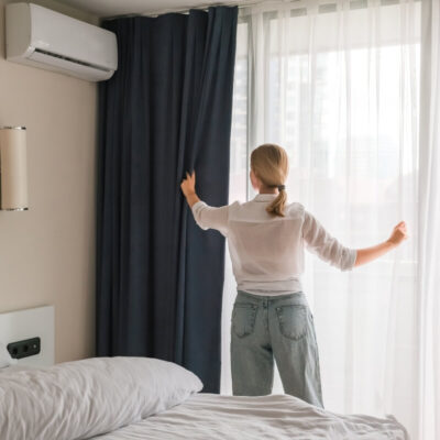 Osoba w sypialni z zasłonami przy oknie oraz klimatyzacją do domu na ścianie.