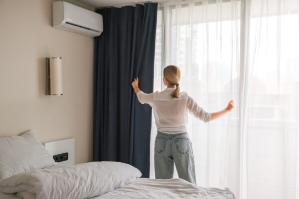 Osoba w sypialni z zasłonami przy oknie oraz klimatyzacją do domu na ścianie.