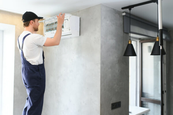 Osoba w kombinezonie przeprowadza montaż klimatyzacji w nowoczesnym wnętrzu.