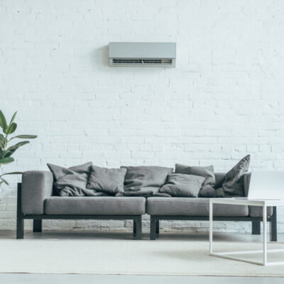 Nowoczesny salon z szarą kanapą, rośliną i biurkiem, gdzie na ścianie zawieszona jest klimatyzacja do domu.