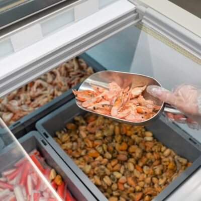 Ręka nabiera owoce morza z zamrażarki z użyciem systemów chłodniczych.