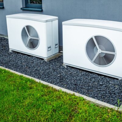 Dwa duże systemy chłodnicze umieszczone na podłożu z czarnych kamieni obok trawnika.