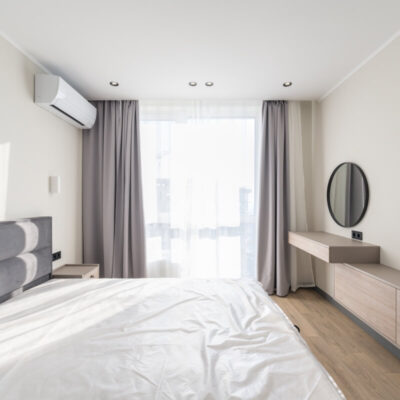 Jasna sypialnia z zasłonami i klimatyzacją na ścianie.