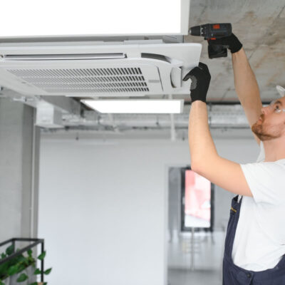 Pracownik w kasku przeprowadza montaż klimatyzacji na suficie.